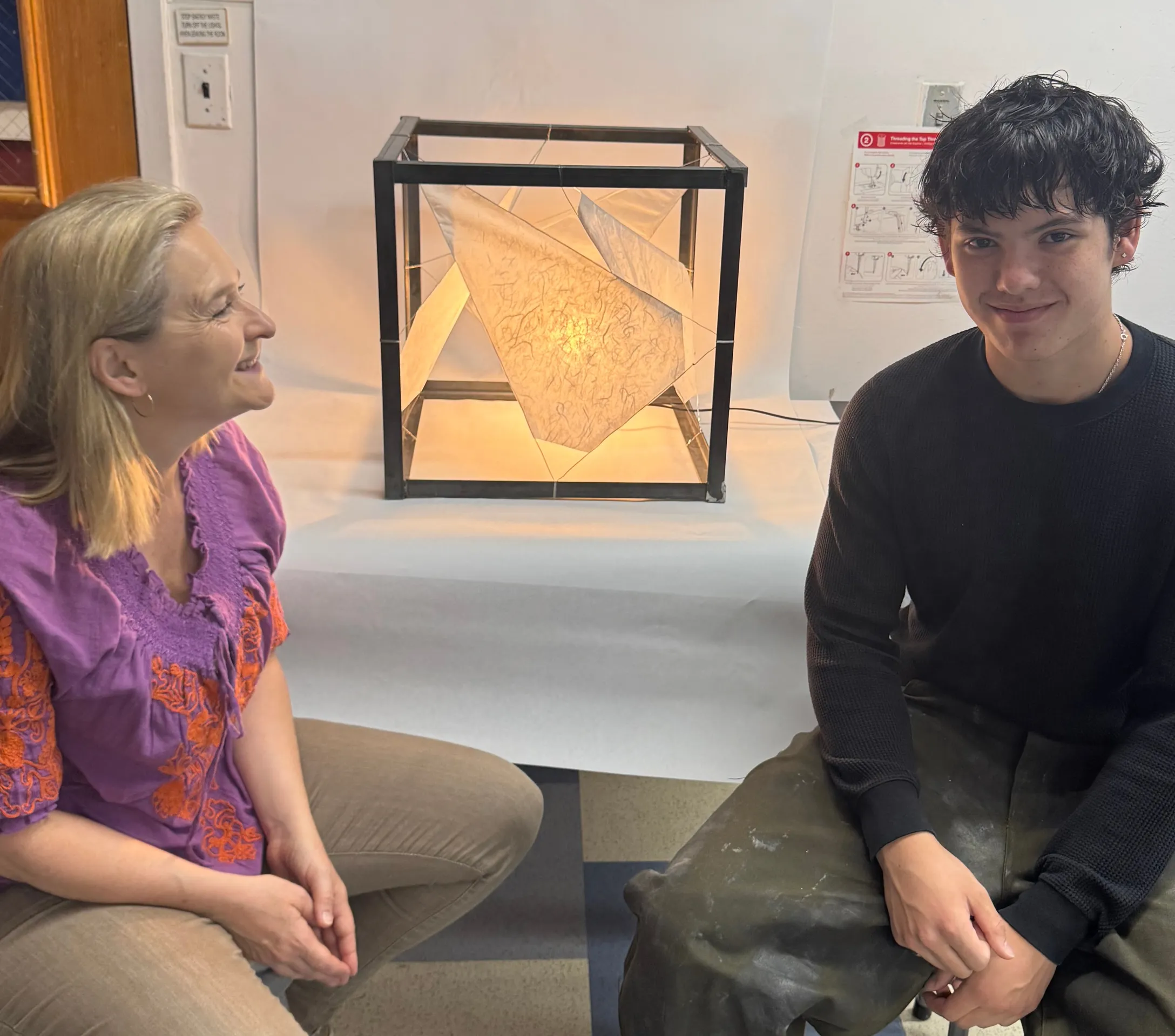 Dr. Nell Daniel and a student sit beside an illuminated cube lamp with translucent panels.