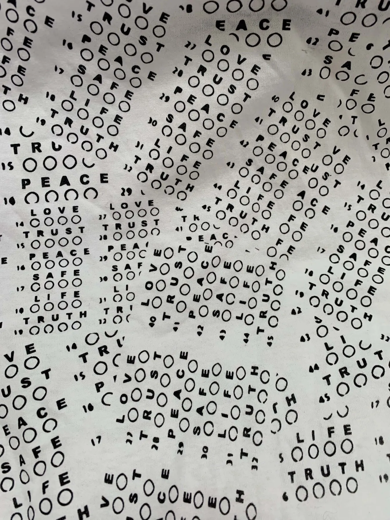 Close-up of white fabric printed with repeated words including PEACE, LOVE, TRUST and TRUTH.